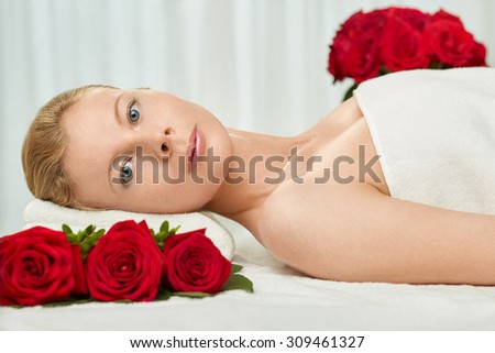 Blond Young Woman Lying on the Back on a Massage Table with Red Roses
