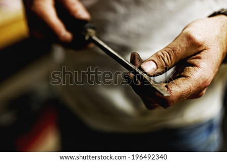 Dirty hands holding on to a screwdriver with both hands.