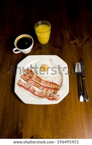 Bacon and eggs on a plate, coffee, and orange juice on a table.