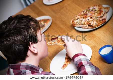 A boy eating pizza and a glass of milk in a blue cup.