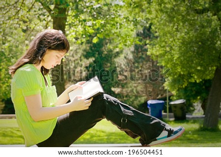 A girl in a green shirt sitting outside reading.