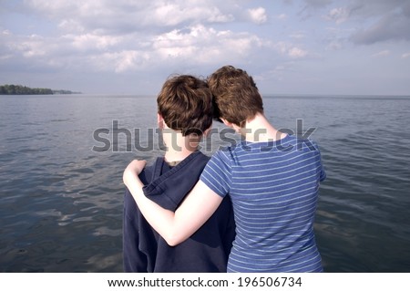 A woman with her arm around the shoulder of an adolescent, looking over the water.