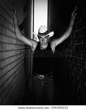 A man in a white cowboy hat and black top, standing in a narrow alley.
