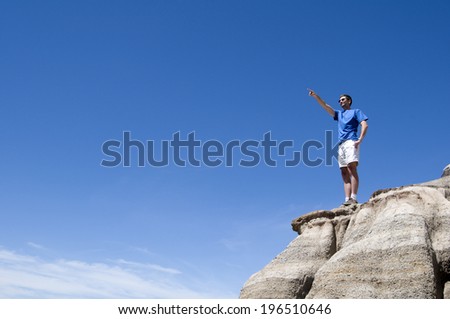 A man stands on a cliff and points at something in the distance.