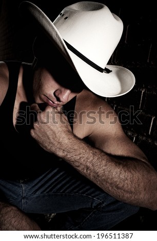 A young man in a sleeveless shirt and cowboy hat strikes a pose.
