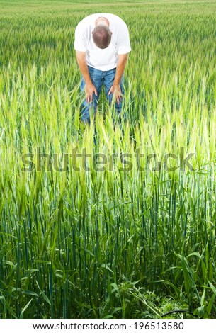 A man bent over looking at the ground in a field of greenery.