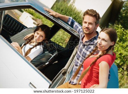 A girl in a car and a guy and girl standing outside the car.