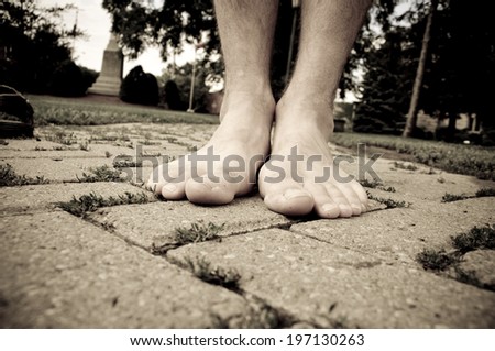 Two bare feet stand on a paved path.