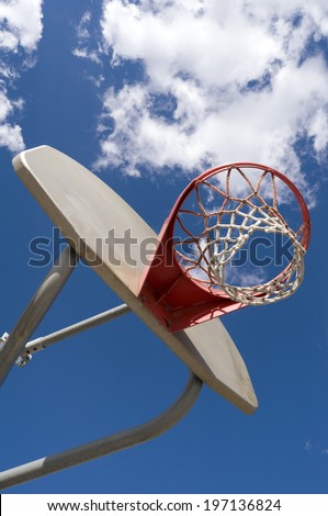 A basketball hoop, net, backboard, and pole with clouds in the sky.