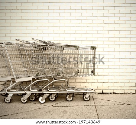 Some shopping carts lined up beside a brick wall.