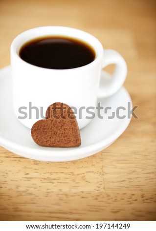 A white mug of black coffee and a heart shaped biscuit.