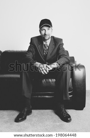 A man wearing a baseball hat sitting on a leather couch.