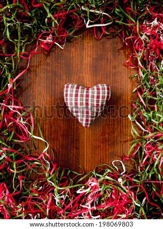A plaid heart on a wood table surrounded by red, green, and white paper shreds.