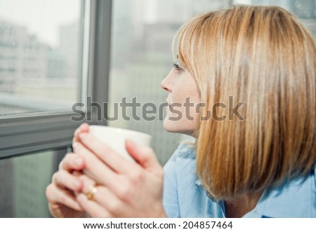 Woman drinking hot beverage by window