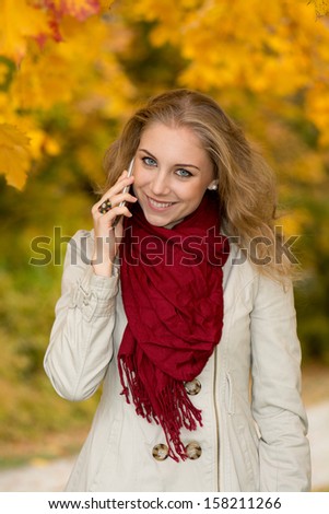 Happy young woman on cell phone in autumn park