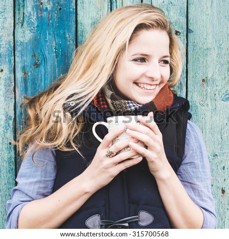 Autumn woman drinking coffee. Fall concept of young woman enjoying hot beverages over blue wooden wall. Caucasian female model in city forest park.