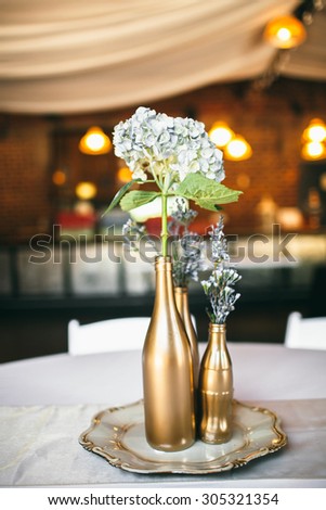 Blue Flower Arrangement in Gold Covered Bottles at Wedding Reception