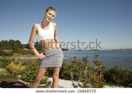 A sexy young woman wearing a skirt and top next to the shoreline.