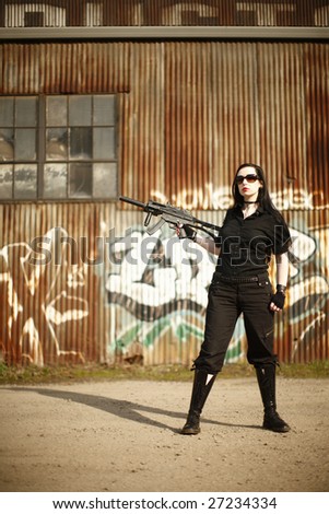 A young woman with a gun dressed in black.