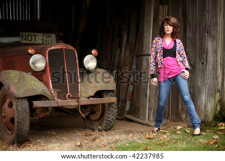 An attractive woman wearing jeans next to barn and an old truck.