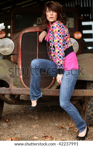 An attractive woman wearing jeans next to an old truck.