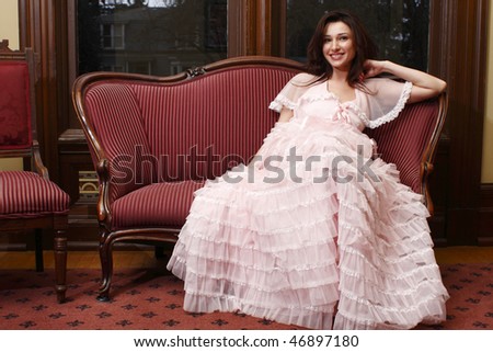 Woman wearing vintage dress sitting on antique sofa.