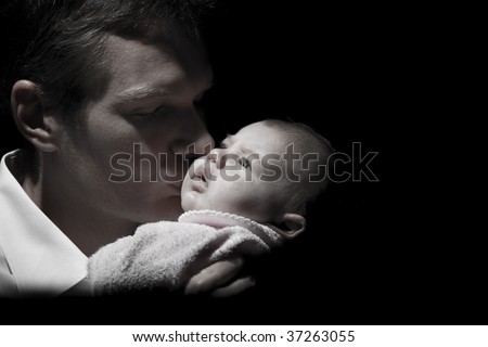 Desaturated capture of a father holding his newborn baby, with light focused on the baby