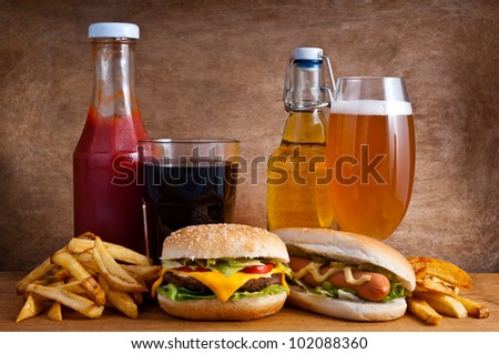 Junk food with burger, hotdog, french fries, cola, ketchup and beer on a wooden background