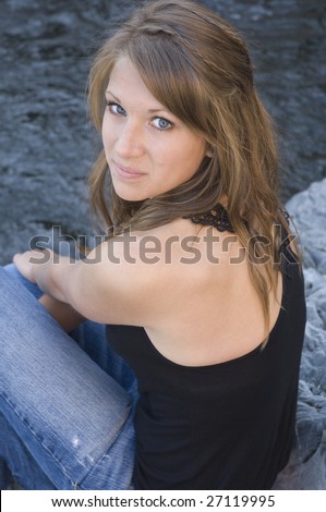 Teenage girl sits on rocks and looks back at the camera with a sweet smile on her face
