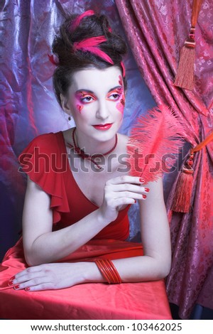 Woman in red. Young lady with artistic make-up and with feathers in her hair.