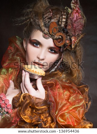 Young stylish lady with artistic make-up and autumn leafs in her hair and  with cake