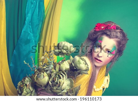 Spring fairy. Young woman in creative image posing with bright fabric's and flowers.