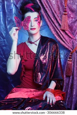 Young lady with artistic make-up and with feathers in her hair and with red butterfly
