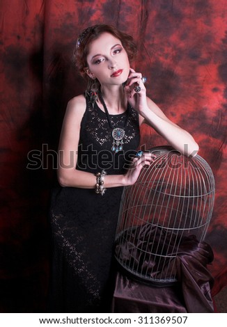 Portrait of young charming woman in ethnic image posing near cage.