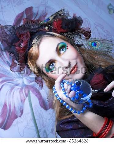 Creative lady in hat with feathers and with loupe and beads.