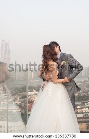 groom kissing bride standing  ouside with huangpu river, traditional Chinese wedding