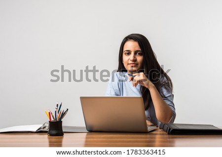 A beautiful and cheerful young Indian Asian woman working on laptop at desk