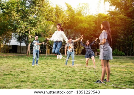 Happy Indian asian young friends playing together with jumping rope outdoors. People playing skipping rope games and laughing outdoors. Happy man or woman jumping over skipping rope held by others