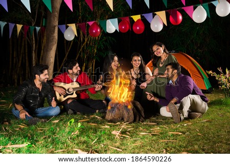 Happy Indian asian friends playing music and enjoying bonfire or campfire in nature