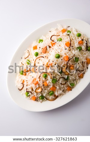 Close up of Delicious Indian Pulav / pilaf / fried rice / veg biryani made up of Basmati rice, vegetable, nuts. served in oval shape ceramic bowl,on white background, top view