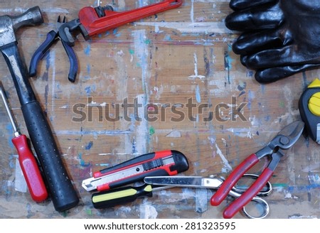 Copy space in the center of a paint stained work surface with tools scattered around. Tools include hammer, screwdrivers, wrench, snipper, plumb bob, gloves, box cutter and scissors.