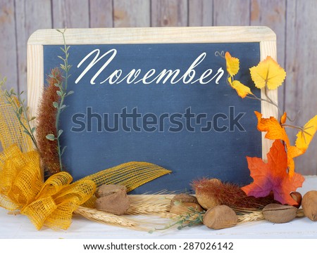 Month of the year for November with seasonally correct items placed around a blackboard with the month written across the top. There is a rustic wood background and copy space on the blackboard.