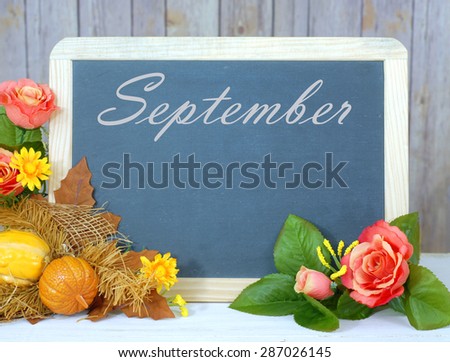 Month of the year for September with seasonally correct items placed around a blackboard with the month written across the top. There is a rustic wood background and copy space on the blackboard.
