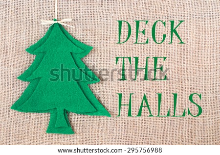 A Christmas tree shape cut out of green felt with round, red felt decorations, topped with a grass bow, is on a natural background. There is a seasonal message added. Rustic, homemade ambiance.