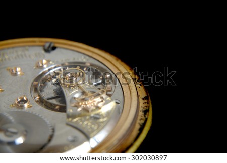 closely cropped close up image of the inner workings of an old, worn antique pocket watch isolated on a black background. The exterior of the watch is visibly worn with age. Copy space upper right.