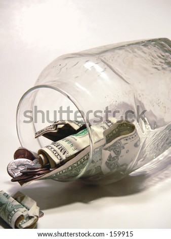 US currency tumbling out of glass jar on neutral background. Vertical image. Concept of having to break into a savings account, could be due to economic recession or downgrade or the last of the money