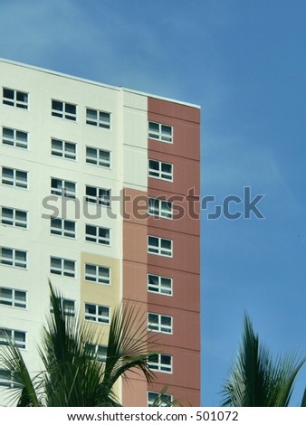 Corner of exterior of generic multi story office, medical or residential building with four colors of paint ranging from light beige to a brick color. The square building enters frame left.  Blue sky.