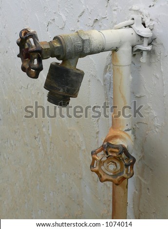 Vertical image of rust stained outdoor garden hose connection and water main with faucet. The rust stain is from lawn sprinklers that are fed by a well and can be seen on the stucco wall and pipes