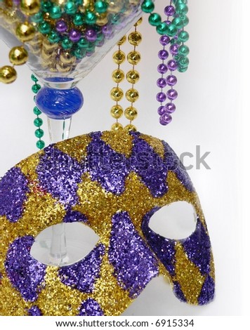 Detail image of purple, green and gold mardis gras beads overflowing a large martini glass with a purple and gold harlequin mask leaning again the glass. Vertical image for party background