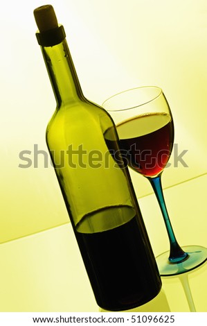 Bottle of red wine with glass on yellow background
